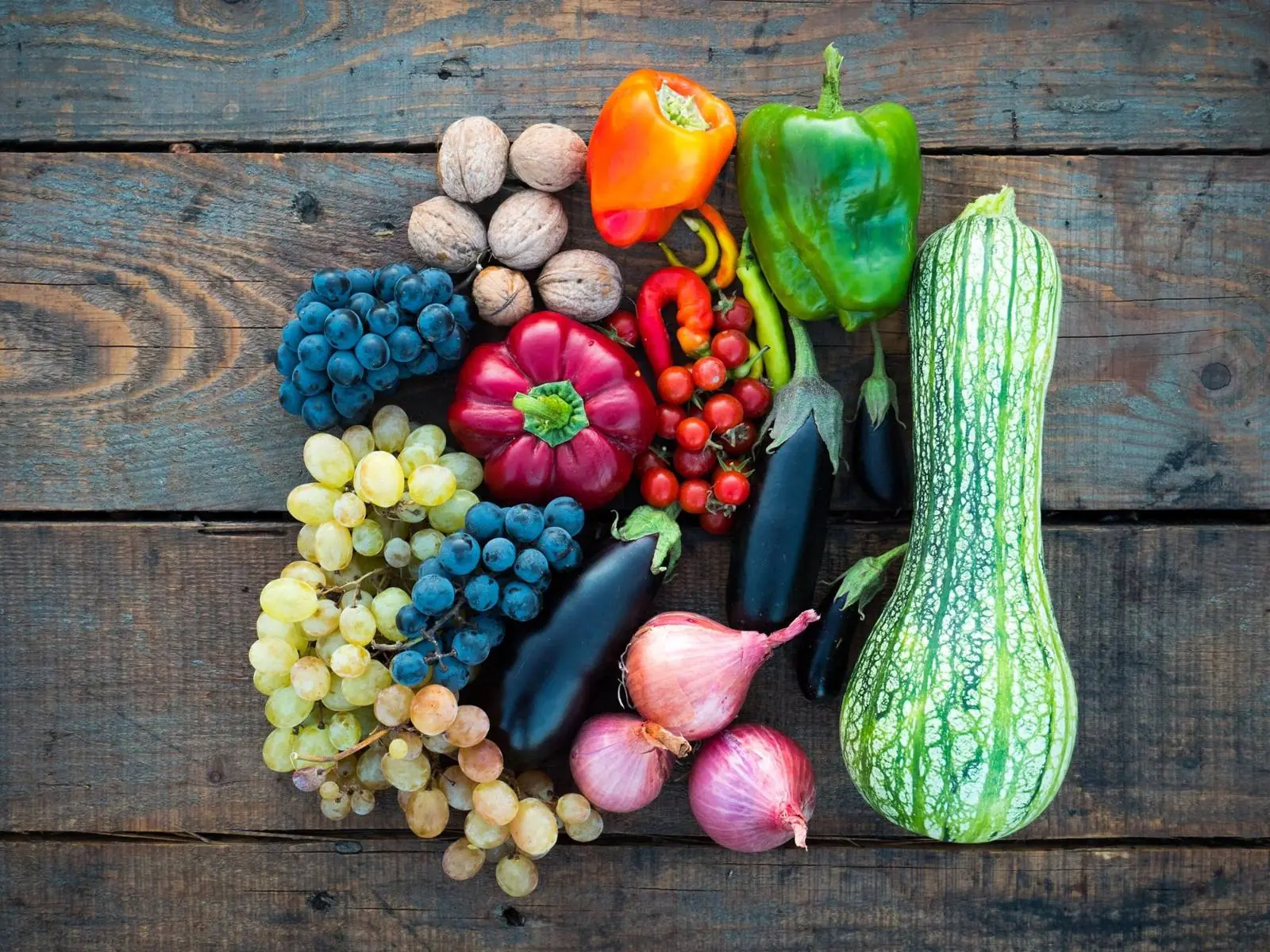 Peppers, grapes, squash and onions arranged on weathered wood